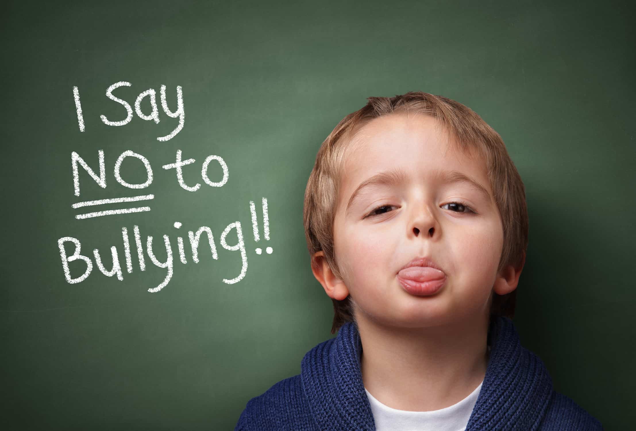 Kid sicking his tongue out in front of a chalkboard that says "I say No to Bullying!"