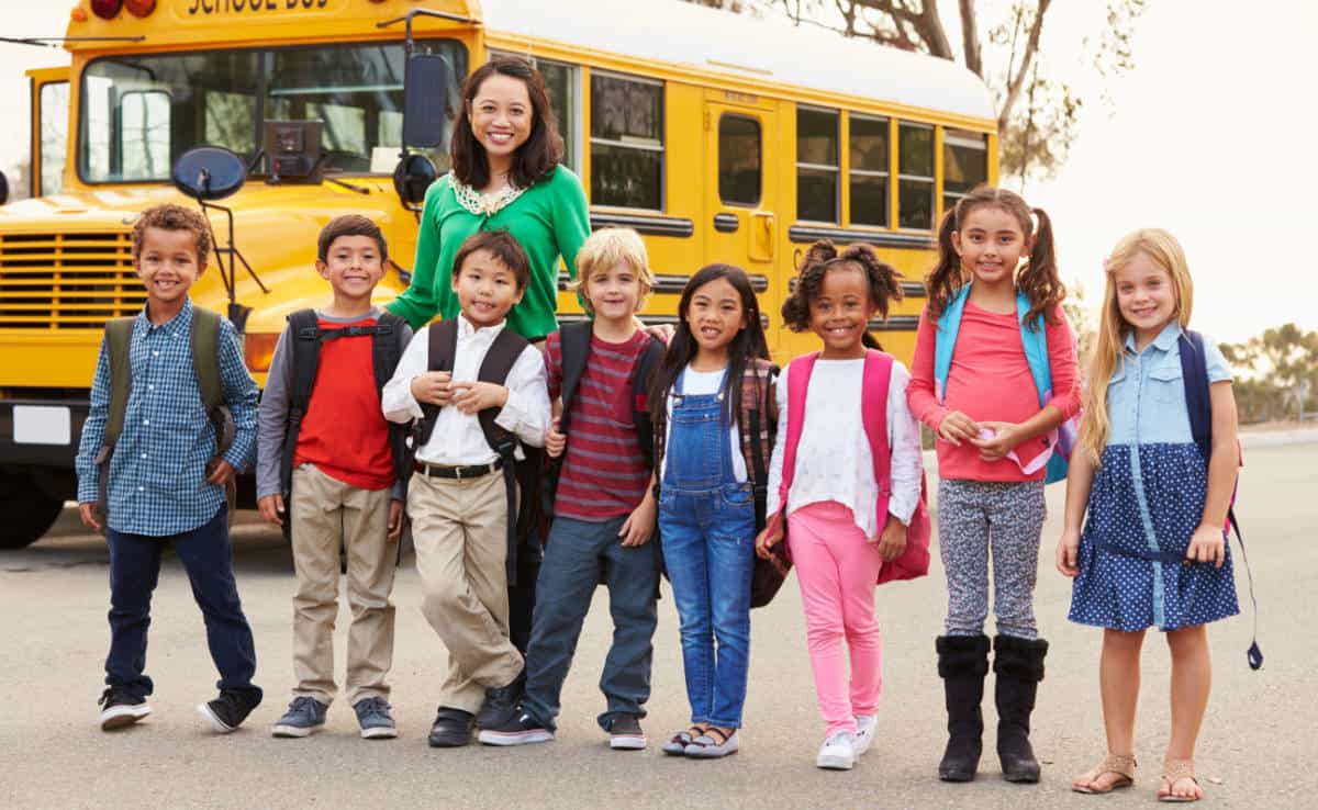 Photo of a teacher and her students in front of a bus